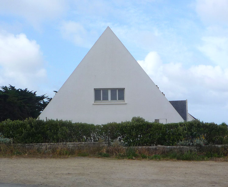 Ein Haus mit spitzem Dach hinter einer Hecke
